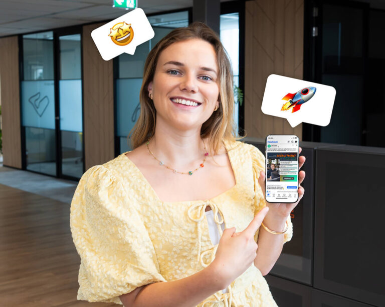 Vrouw wijst lachend naar haar telefoon met een succesvolle Facebook vacatureadvertentie